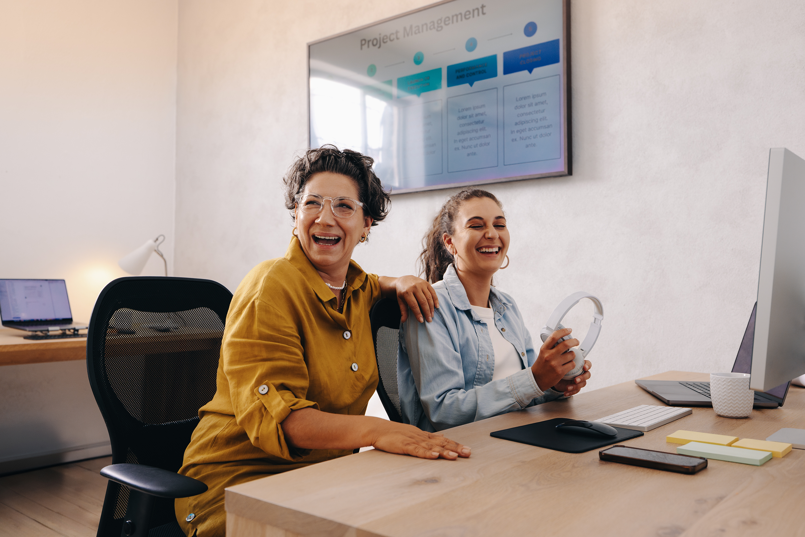 Two smiling colleagues talking at a desk